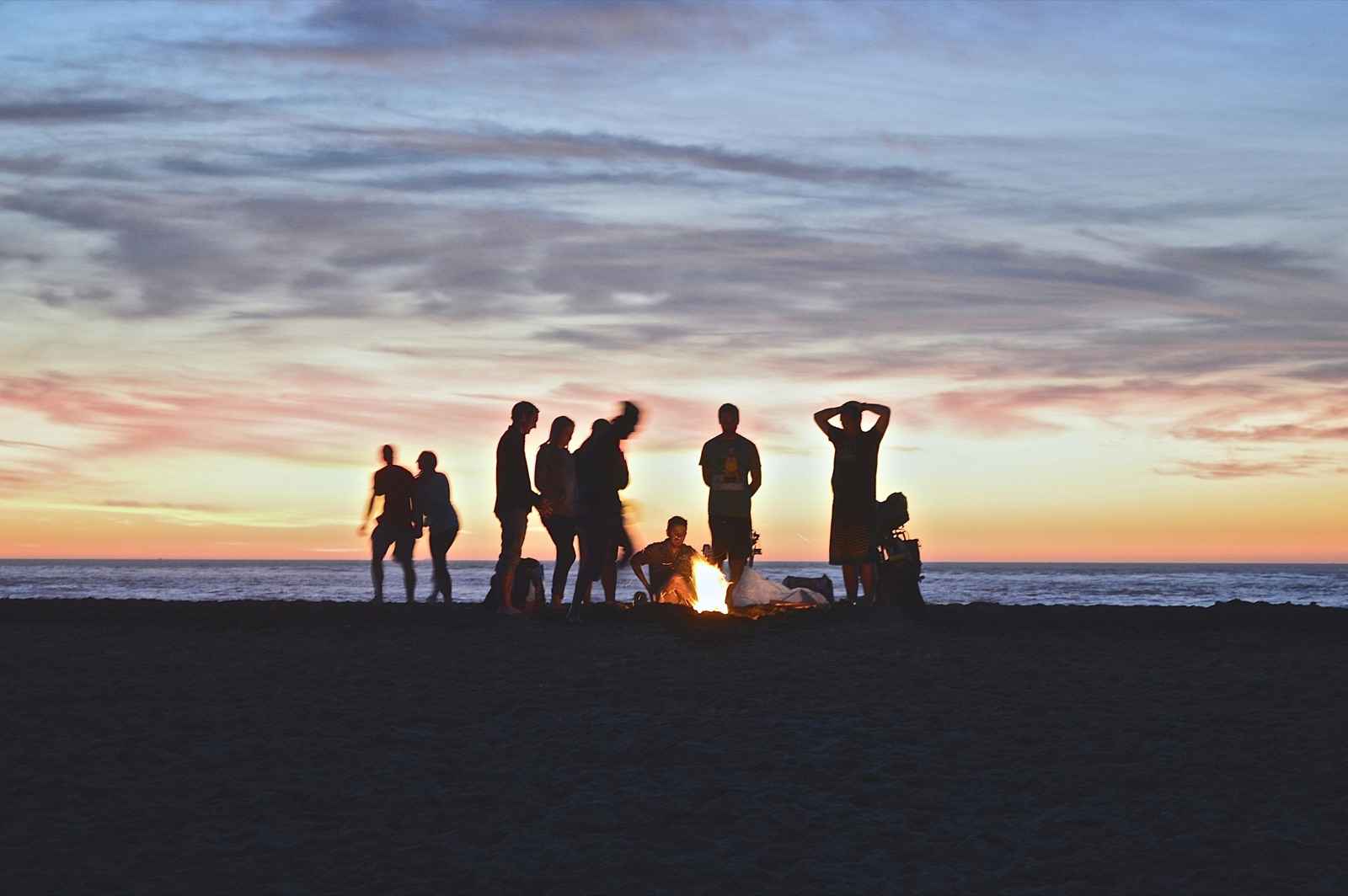 Friends gathered around a beach fire at sunset